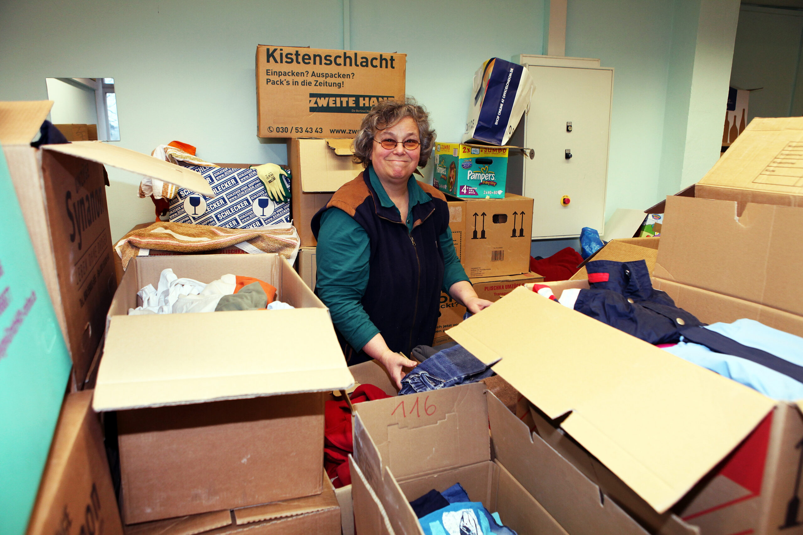 Eine ehrenamtliche Helferin sortiert Kisten in der Kleiderkammer.